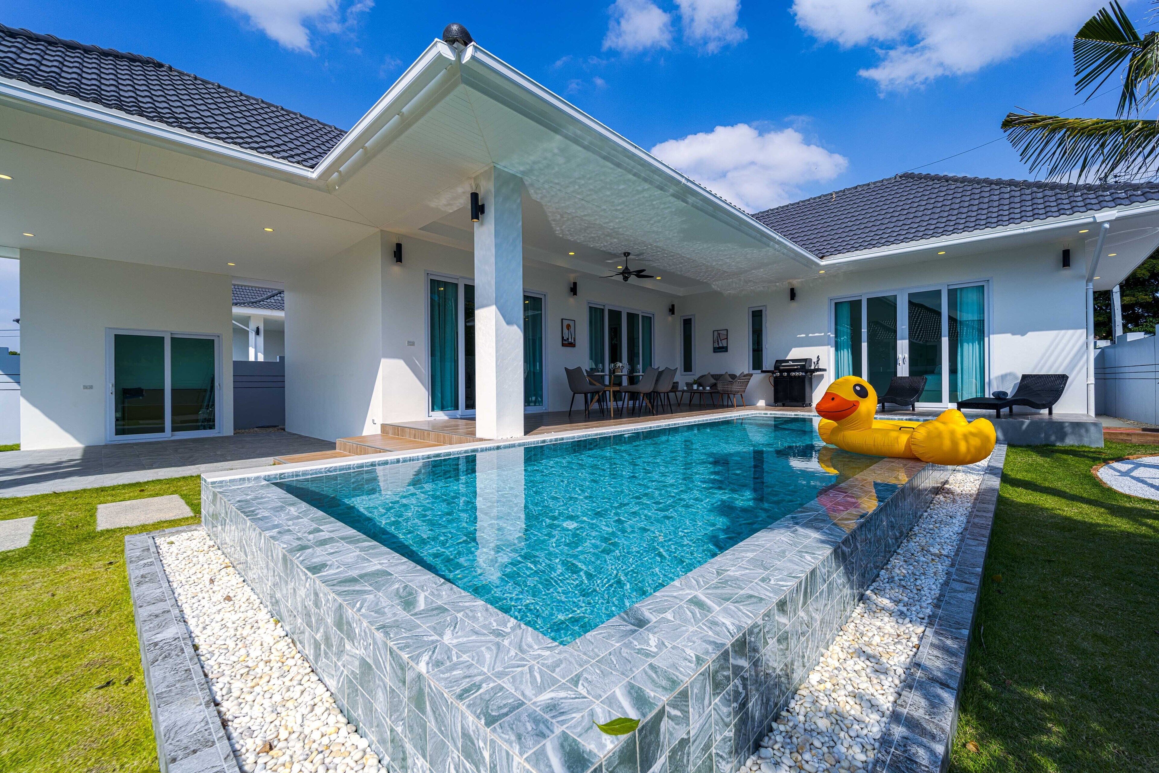 A modern house with a swimming pool, a patio with outdoor furniture, and a duck float.