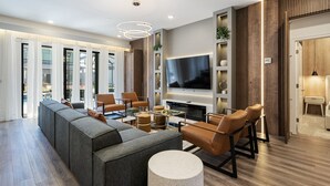 A modern living room with a sectional sofa, leather armchairs, a coffee table, and a flat-screen TV mounted on the wall.