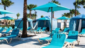 A poolside area with blue lounge chairs and umbrellas, palm trees, and a clear sky. - Last Minute Disney Getaway! Private Pool & Themed Bedrooms. Book Now! #56089 (Orlando)