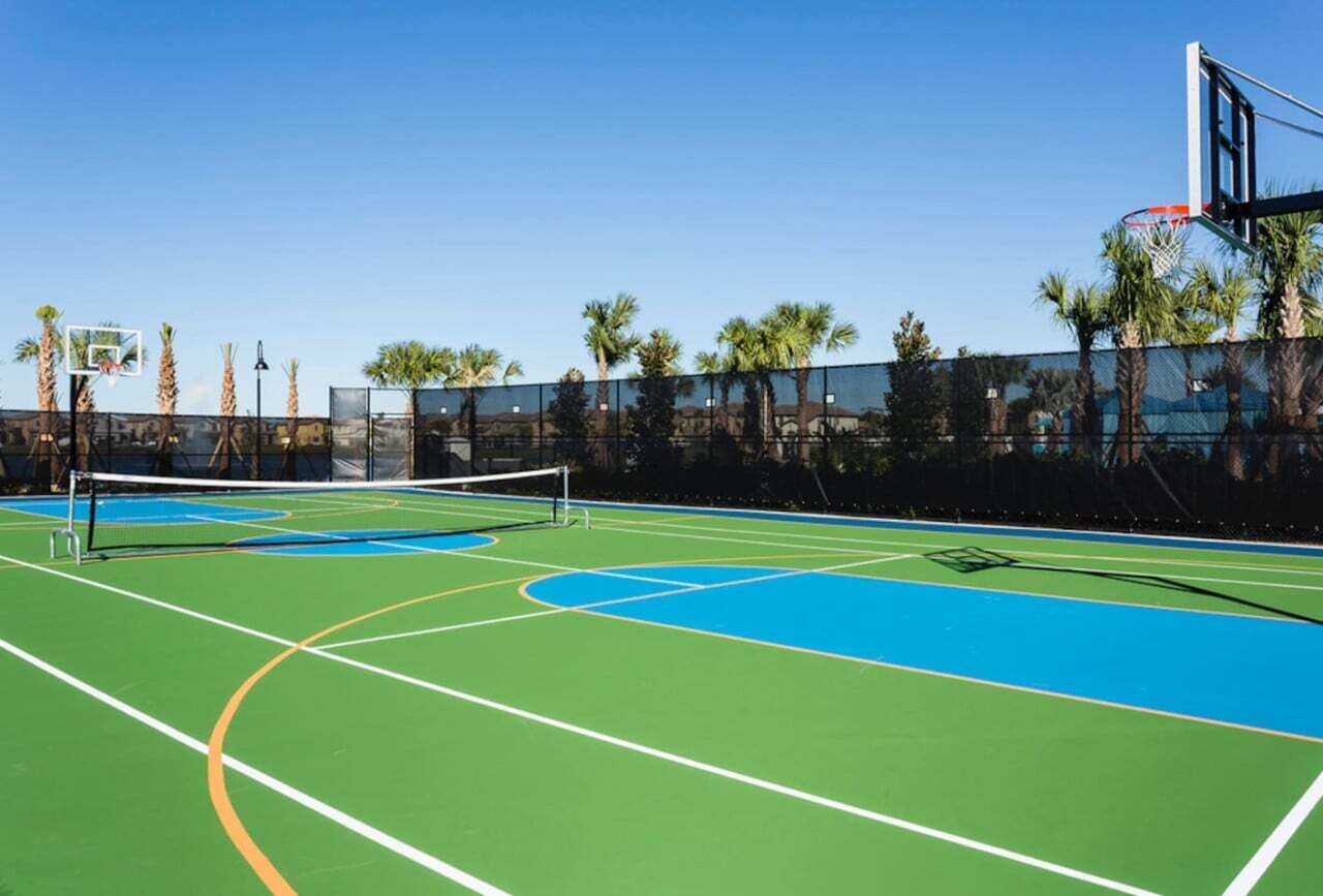 Een buitenbasketbalveld met een net, omringd door palmbomen en een hek.