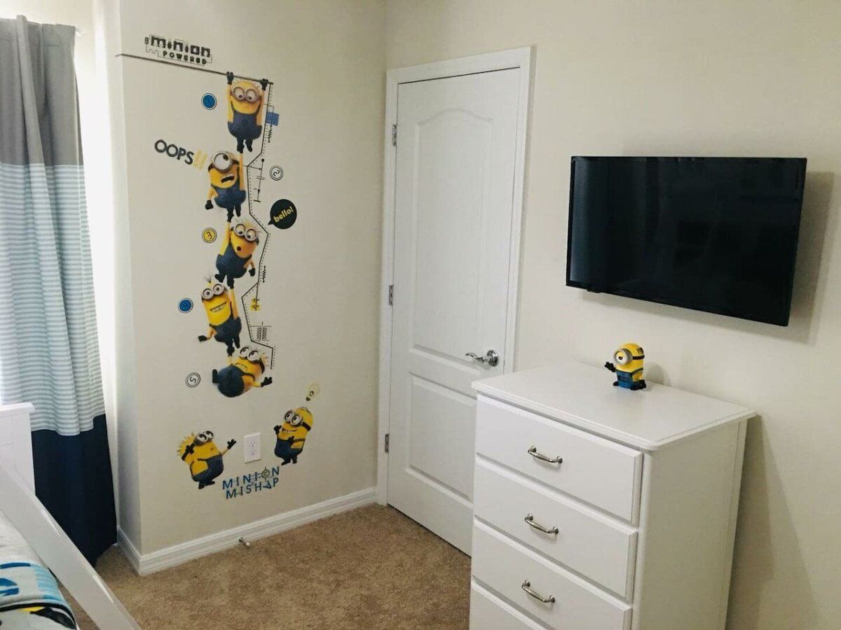 Ein Schlafzimmer mit weißem Schminktisch, einem an der Wand montierten Fernseher und einer Wandsticker-Motiv aus Minions.