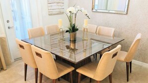 A dining area with a glass-top table surrounded by six beige upholstered chairs. - Last Minute Disney Getaway! Private Pool & Themed Bedrooms. Book Now! #56089 (Orlando)