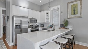 Una cocina moderna con armarios blancos, electrodomésticos de acero inoxidable, una isla grande con taburetes de bar y una lámpara colgante.
