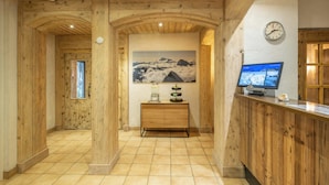 A wooden interior with a reception desk, a clock, and a mountain painting. - Hotel Sarazena (Zermatt)