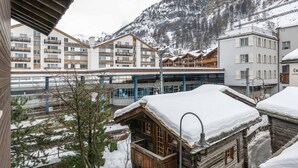 A snowy mountain town with wooden buildings and a modern hotel in the background. - Hotel Sarazena (Zermatt)