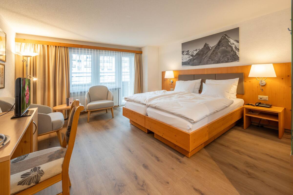 A hotel room with a double bed, a desk with a chair, a small table, and a television.