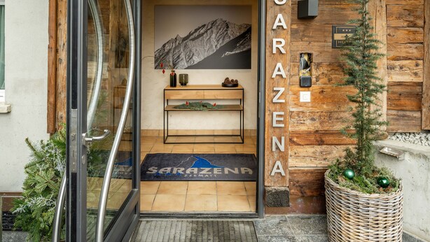 A hotel entrance with a wooden facade, a mountain view, and a reception desk. - Hotel Sarazena (Zermatt)
