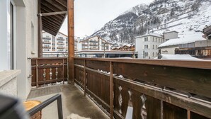 A balcony with a wooden railing overlooking a snowy mountain and buildings. - Hotel Sarazena (Zermatt)
