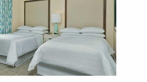 A hotel room with two single beds, a nightstand with a lamp, and a patterned wall.