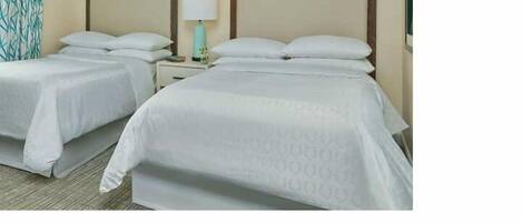 Habitación de hotel con dos camas individuales, una mesita de noche con lámpara y un papel tapiz estampado.