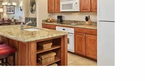 A kitchen with wooden cabinets, a granite countertop, a built-in dishwasher, and a white refrigerator.