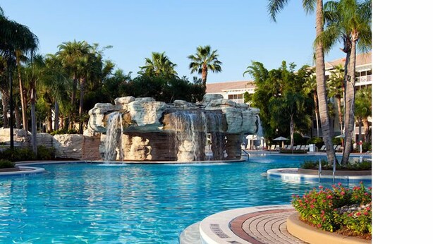 A pool with a rock formation, palm trees, and a building in the background.