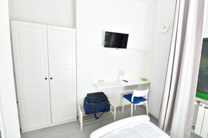 Une chambre à coucher comprenant un lit, un bureau avec une chaise, une télévision et une armoire.