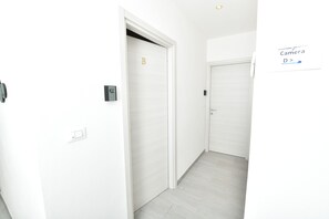 A hallway with white walls and doors, a sign indicating a camera direction, and a light switch.