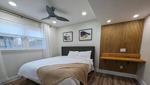 A bedroom with a bed, a ceiling fan, a window with blinds, and a wall-mounted shelf.