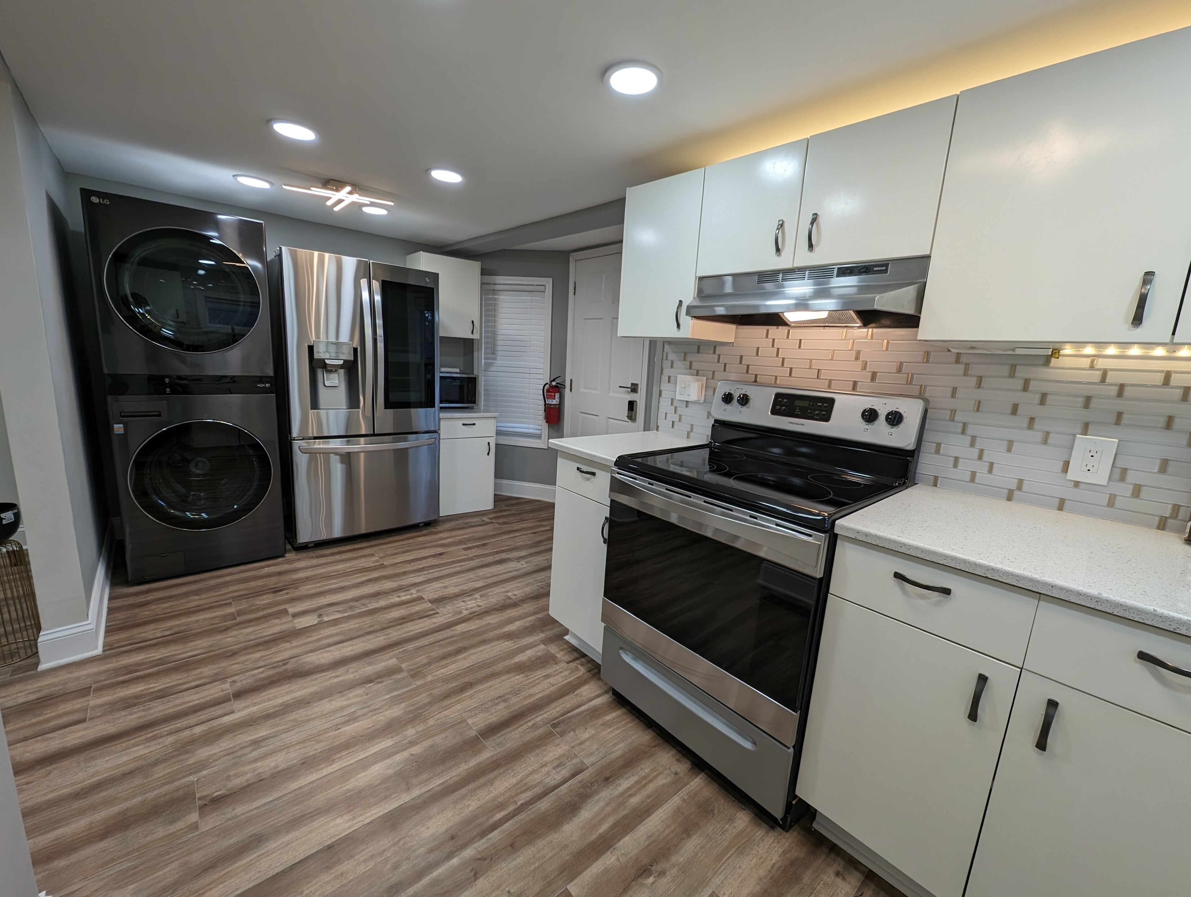 A modern kitchen with stainless steel appliances, white cabinetry, and a wooden floor.