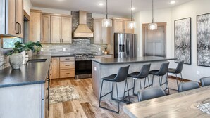 A modern kitchen with wooden cabinets, a stainless steel refrigerator, and a bar area with stools. - Incredible New 3200+ Sq. Ft. Lodge w/ Arcades, Shuffleboard, Hot Tub, Paved! (Lead)
