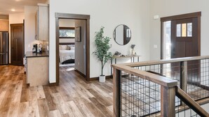 A modern interior with a wooden floor, a kitchen with a refrigerator, a dining area with a table and chairs, and a staircase with a railing. - Incredible New 3200+ Sq. Ft. Lodge w/ Arcades, Shuffleboard, Hot Tub, Paved! (Lead)