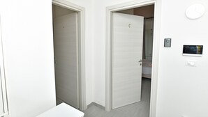 A hallway with two doors, one closed and one open leading to a bathroom. There is a small table and a wall-mounted light switch. - Double room with private bathroom (San Lazzaro di Savena)