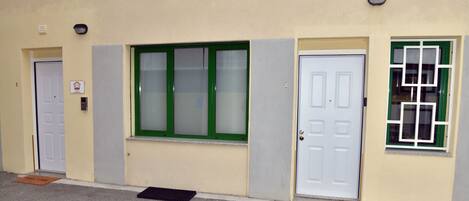 A building with three doors, each with a different window design. There are two doormats on the ground.