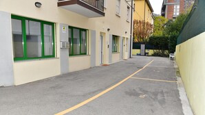 Un espace de stationnement avec des places délimitées, un bâtiment aux fenêtres encadrées de vert et un vélo appuyé contre le mur.