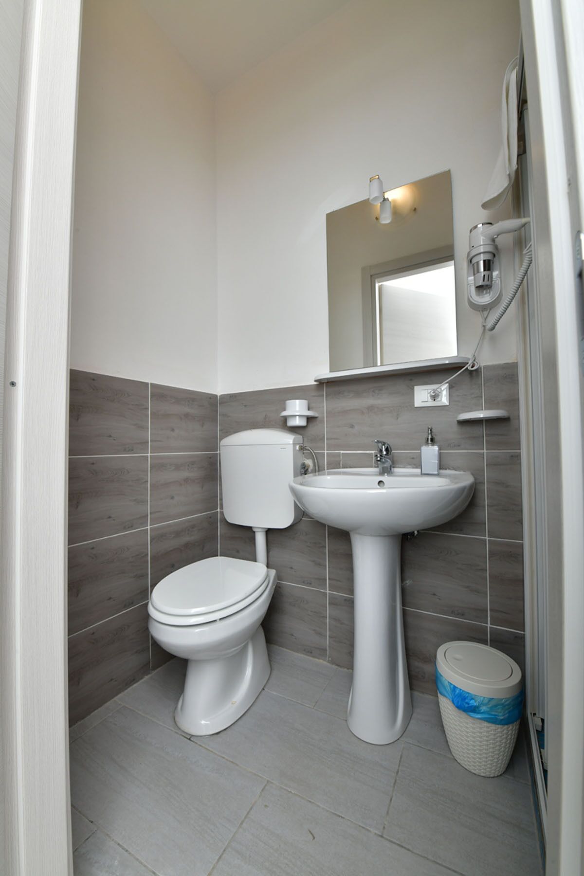 A compact bathroom with a toilet, sink, and a trash bin.