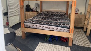 A bunk bed with a red blanket, a patterned quilt, and a small desk with a lamp. - Our Rustic off grid Serenity Camp is 190 sq ft and 2300 feet through the woods. (Unadilla)