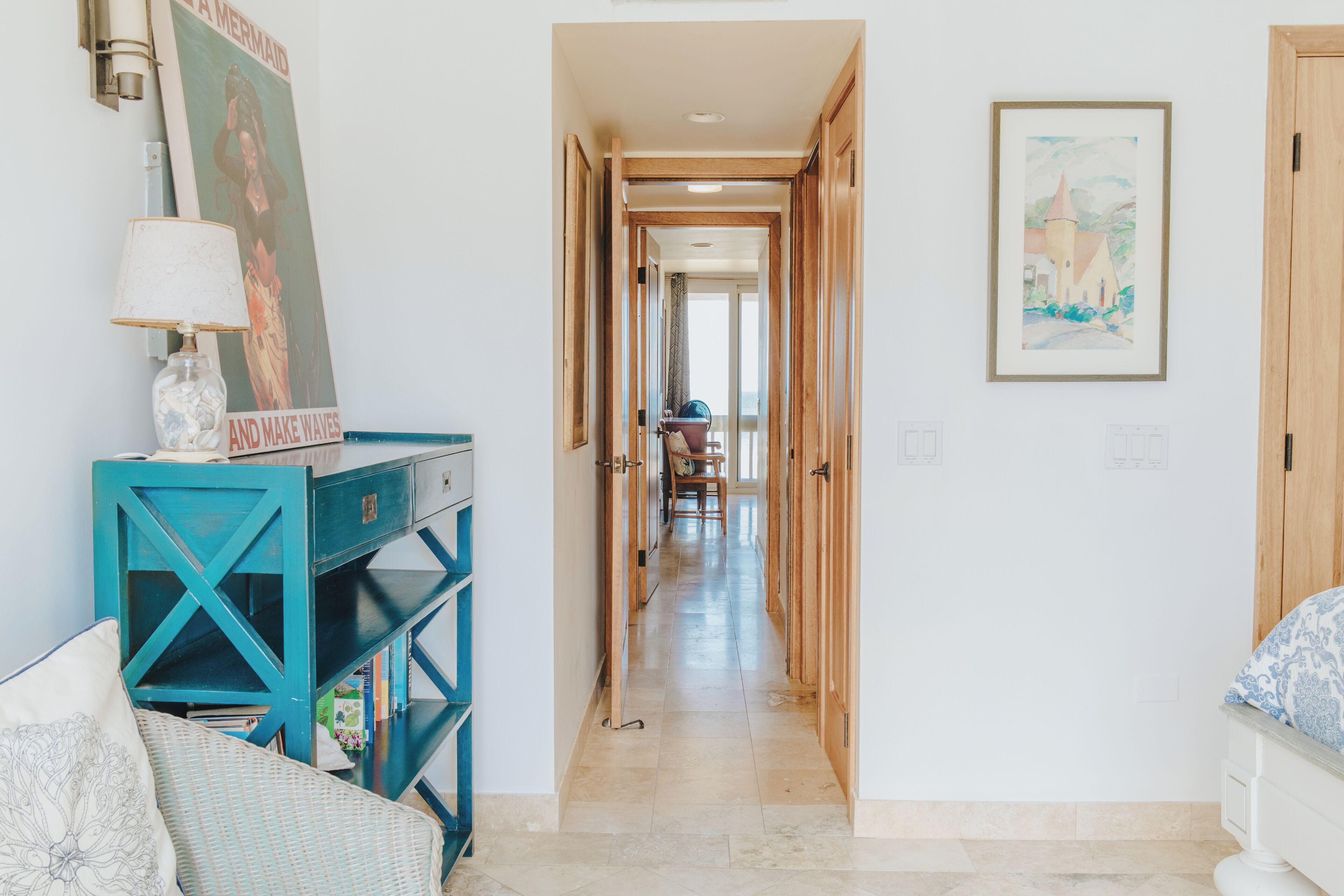 Un couloir avec une console de couleur turquoise, une affiche et un tableau encadré accroché au mur.