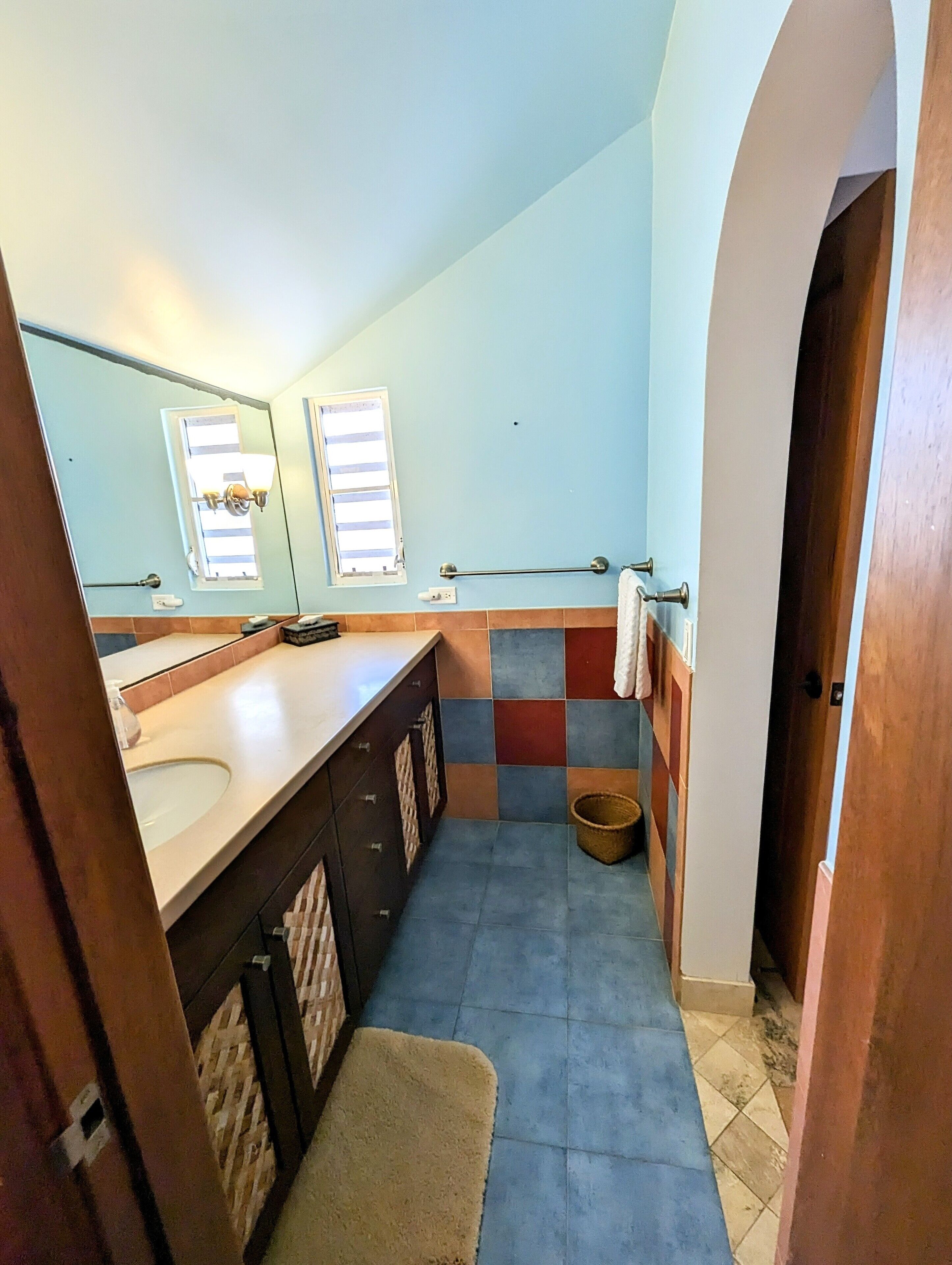 Un baño con un espejo grande, dos lavamanos, un perchero para toallas y una ventana pequeña.