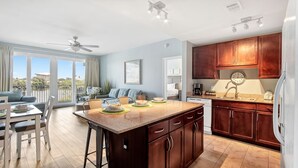 A modern kitchen with dark wood cabinets, a granite countertop, and a dining area with a table and chairs. - Lake balcony condo w/ daily attraction perks (Panama City Beach)