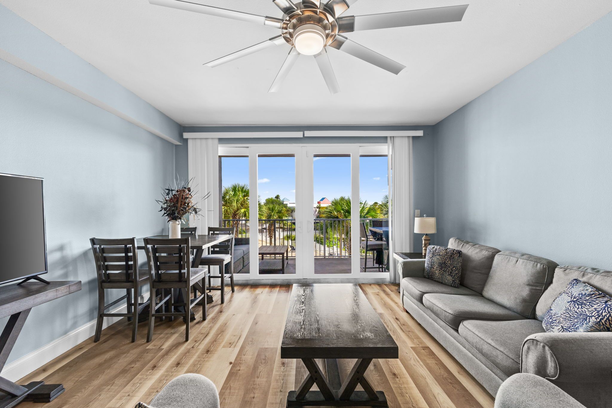 A modern living room with a flat-screen TV, a sofa, a coffee table, and a dining area with chairs and a table.