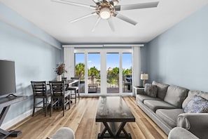 A modern living room with a flat-screen TV, a sofa, a coffee table, and a dining area with chairs and a table.