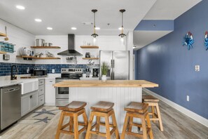 Una cocina moderna con una isla central, taburetes de bar, electrodomésticos de acero inoxidable y decoración en la pared.