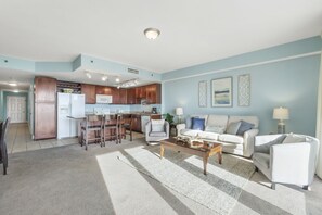 Uma sala de estar moderna com sofá, mesa de centro e área de cozinha com armários de madeira e geladeira.