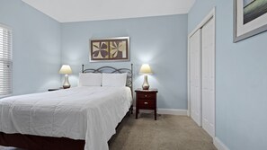 A bedroom with a bed, two bedside tables with lamps, a nightstand, a framed artwork above the bed, and a closet. - Waterfront condo w/ daily attraction tickets (Panama City Beach)
