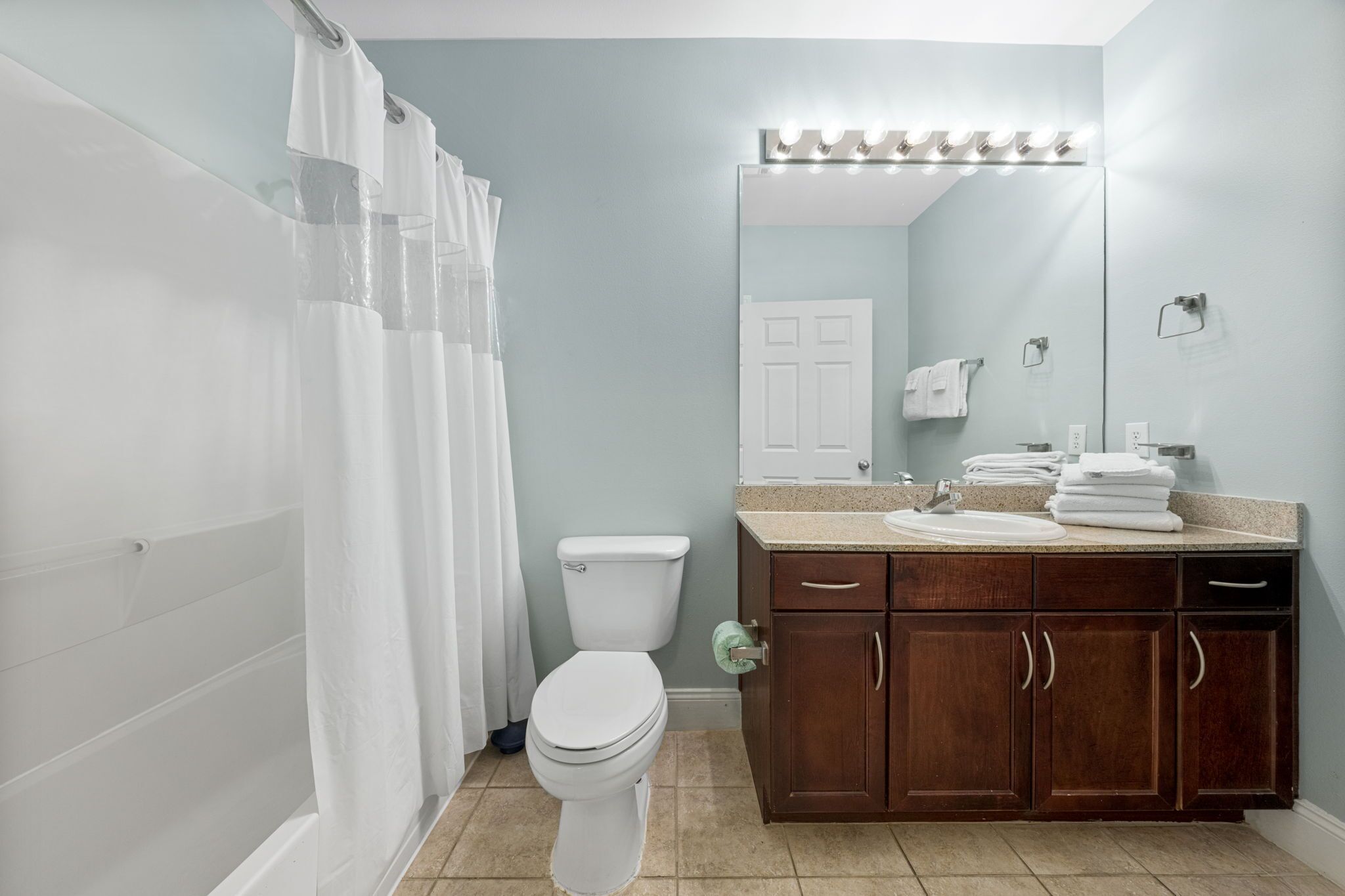 A bathroom with a shower curtain, a toilet, a sink with a mirror, and a vanity with cabinets.