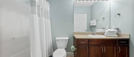 A bathroom with a shower curtain, a toilet, a sink with a mirror, and a vanity with cabinets.