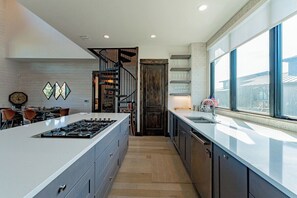 A modern kitchen with a central island, a built-in stove, and a large window providing a view of the outside. - Lola's Lakefront: 3-Bed Treehouse with Porch, Fire Pit & Year-Round Fun (Spicewood)