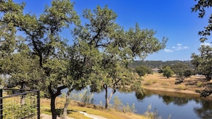 A pathway alongside a calm body of water with trees and a clear sky. - Lola's Lakefront: 3-Bed Treehouse with Porch, Fire Pit & Year-Round Fun (Spicewood)
