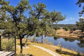 A pathway alongside a calm body of water with trees and a clear sky. - Lola's Lakefront: 3-Bed Treehouse with Porch, Fire Pit & Year-Round Fun (Spicewood)