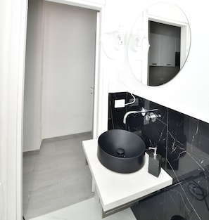 A modern bathroom with a black vessel sink, a white countertop, and a mirror above the sink.