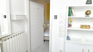 A hallway with a white radiator, a door leading to a bedroom, and a white shelf with books and a globe.