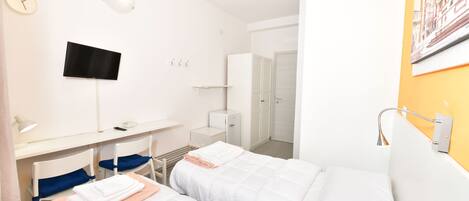 Une chambre d’hôtel avec deux lits, un bureau avec un ordinateur, une télévision et une salle de bain avec un mur orange.
