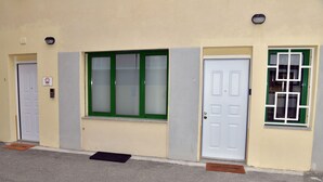 A building with three doors, each with a different window design. There are two doormats on the ground.