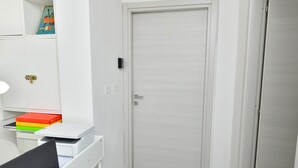 Une pièce avec une porte fermée, un bureau avec un ordinateur portable et une étagère remplie d’objets colorés.