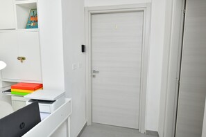 Una habitación de hotel con un escritorio blanco, una computadora portátil y una puerta cerrada.