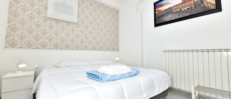Une chambre d’hôtel avec un lit, une table de chevet, un tableau accroché au mur et un radiateur.