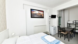 A hotel room with a bed, a desk, a chair, a small refrigerator, a clock, and a picture on the wall. - Family Room with private bathroom (San Lazzaro di Savena)