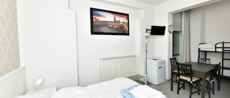 Une chambre d’hôtel avec un lit, un bureau, une chaise, un radiateur, une télévision et un tableau au mur.
