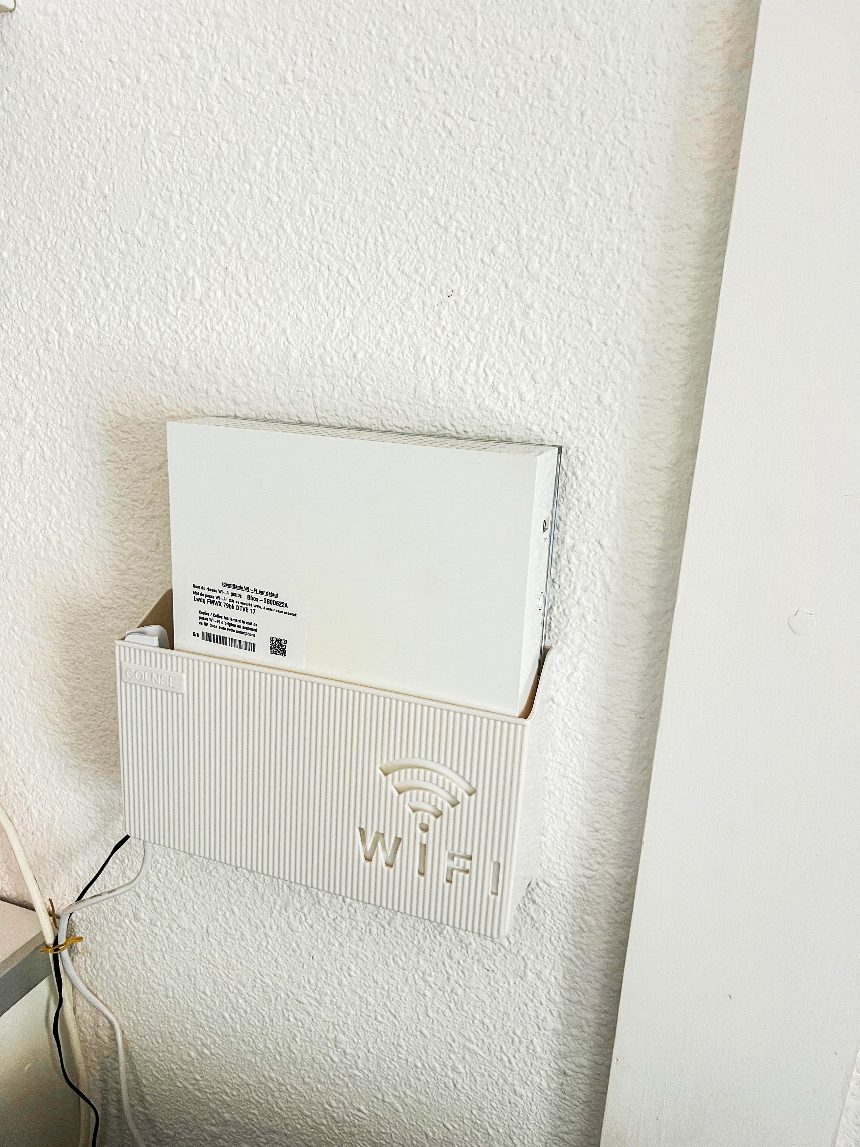 A white textured wall with a white box mounted on it, containing a label and a Wi-Fi symbol.